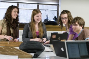 Students work together in a group around laptop computers